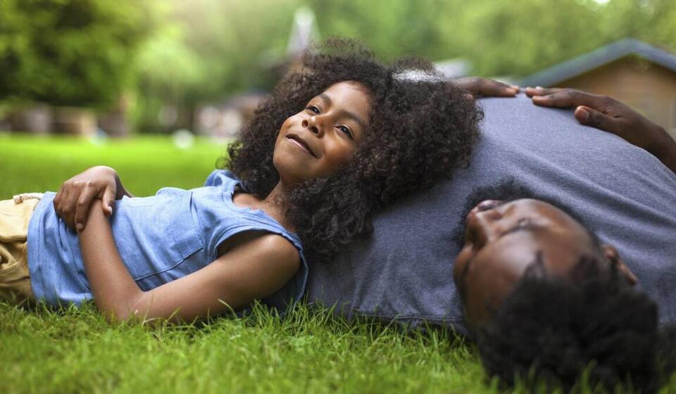 A young girl reclines against her father's shoulder on fresh grass