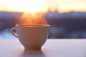 Coffee cup on table with steam and sunrise in the background.